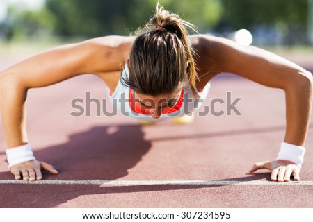 Focused young beautiful woman doing push-ups outdoors on a hot summer day