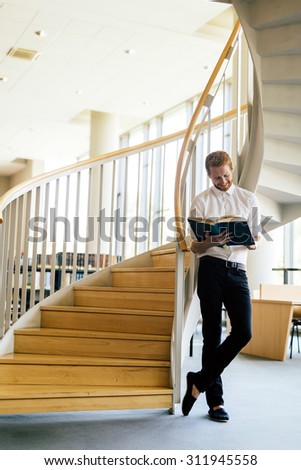Handsome smart guy reading a book in a library