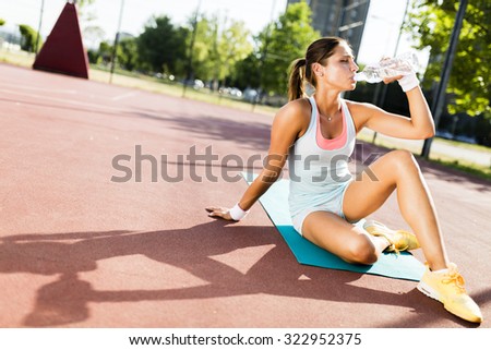 Young beautiful woman drinking water after exercise in a city training court on a sunny day