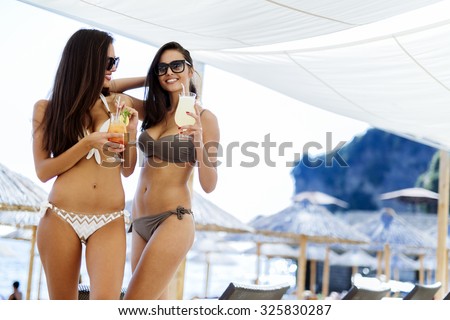 Girls drinking cocktails on beach in bikinis