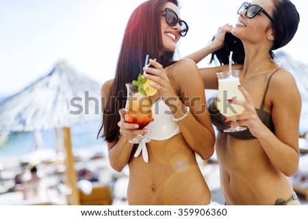 Girls drinking cocktails on beach in bikinis