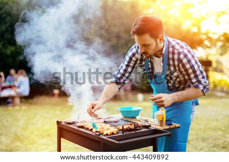 HAndsome male preparing barbecue outdoors for friends