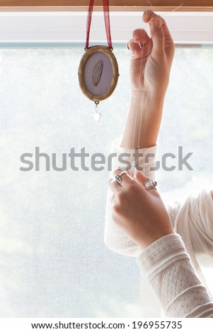 Woman holding glass prism near window reflecting rainbow light onto hands.