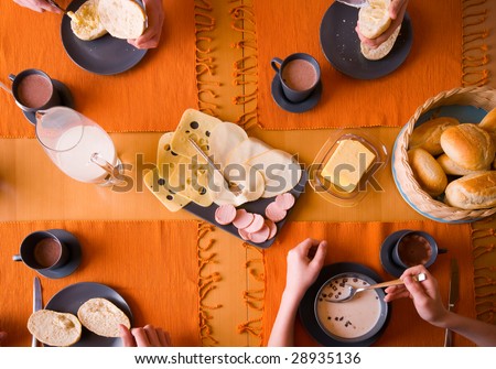 A view from the top of a table with a typical german breakfast. Four person are having a meal.
