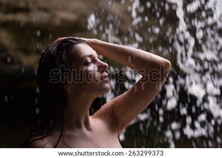 Outdoor photo of sexy beautiful woman with brunett hair in bikini relaxing under a waterfall