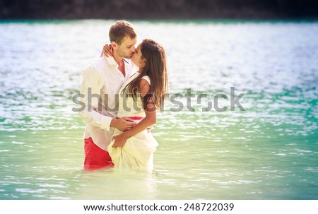 brunette girl with handsome man stand in sea water in island bay with green mountain background