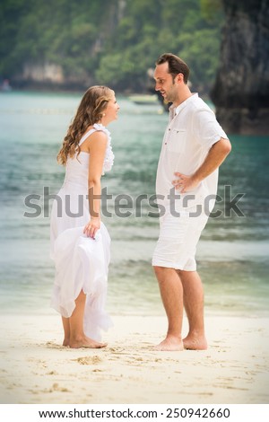 pretty blonde bride and handsome groom talk standing at sand beach against azure sea background