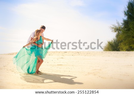 handsome man hold his beautiful blonde wife in elegant dress on island beach