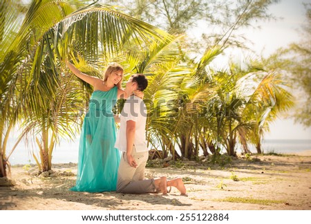beautiful blonde woman in elegant dress kiss her handsome husband stand in green palm leafs