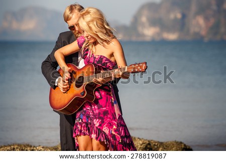 blonde girl in red with  guitar by bearded guitarist on beach at low tide