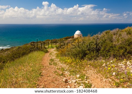 View of mountain road with trees, cloudy sky, Mediterranean sea and Christian Chapel on the background