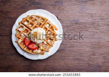 golden waffle with ice cream and caramel sauce and sliced fresh red strawberries sprinkled with sugar on a wooden table