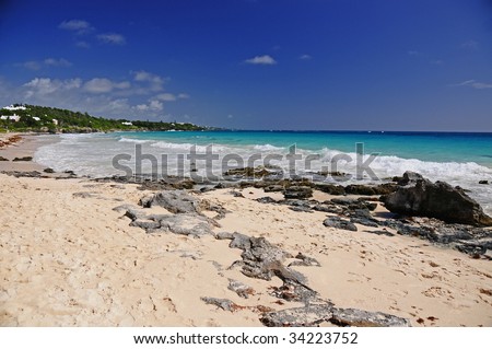 Bermuda beach during a hot summer day.  Photo includes the sky, rocky coastline, pink sand and the tide rolling in.