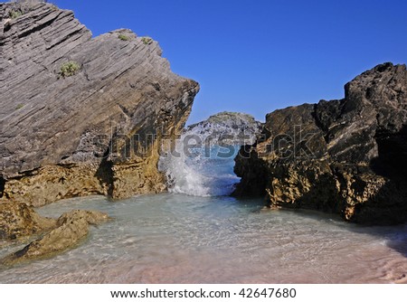 Bermuda\'s Horseshoe Bay beach during a hot summer day.  Photo includes the sky, rocks, pink sand and a wave rolling in.