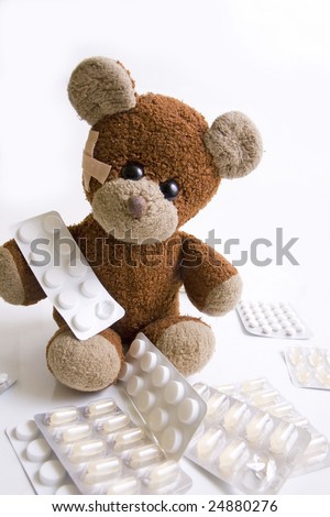 A sick teddy bear is sitting between pills. Adhesive bandage in his face.