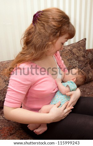 Mother in nursing bra and pink blouse holding in her arms and nursing ( breast feeding ) her newborn baby dressed in teal body.