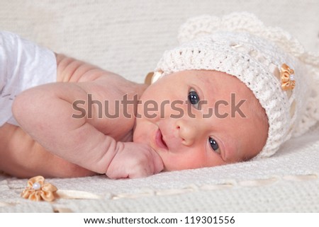 10 day old newborn baby in white fashion knitting hat lying on the tummy on white knitting blanket and looking at the camera. Selective focus on baby face