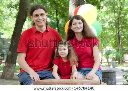 Summer portrait of happy smiling family dressed in red with bunch of balloons behind
