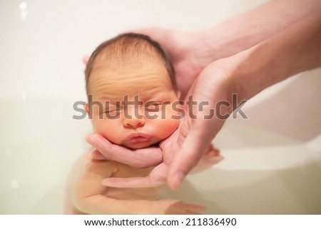 5 days old newborn baby swimming with help of parents hands for the first time. Baby has neonatal jaundice. Focus on baby head