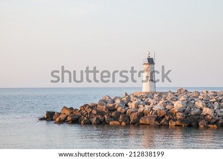 Old lighthouse with solar battery on stone seaside at dusk.