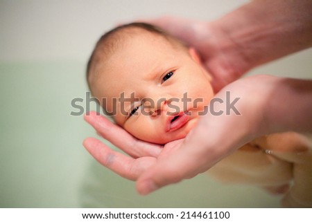 Newborn baby swimming with help of parents hands for the first time. Baby has neonatal jaundice. Focus on baby head