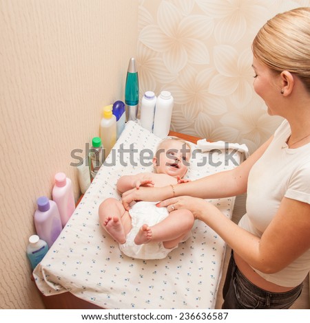 Mother getting dressed her baby on the changing diaper table
