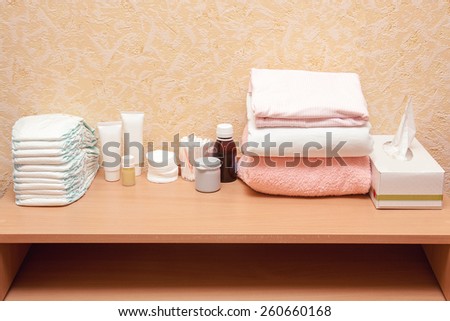 Baby care essentials on the diaper table: diapers, cream, napkins, bottles, oil, cloth and towel