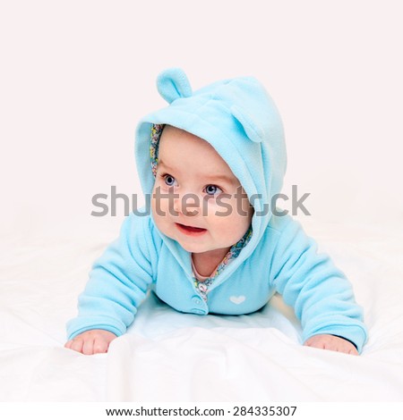 Little baby in turquoise clothes lying on his tummy with his head up on light pink sheet background. Selective focus on baby face.