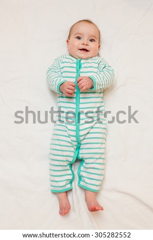 Cute laughing baby  in striped sleep suit lying on his back on white sheet. Baby looking straight at the camera.