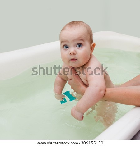 Funny chubby baby taking a bath with the help of parents hands. Baby looking straight at the camera. Selective focus on baby head.