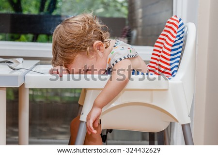 Tired child sleeping in highchair after the lunch. Baby over eating and fall asleep just after feeding, lying his face on the table tray.