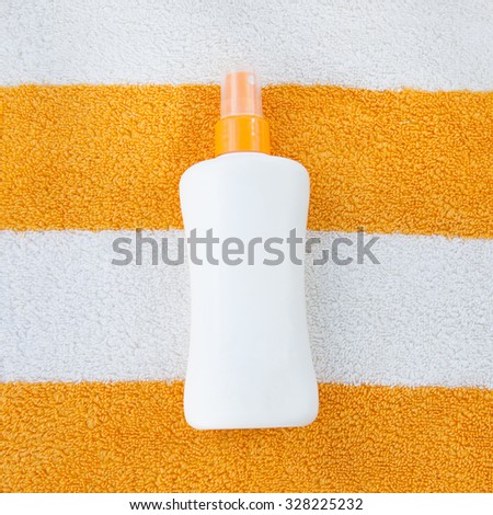Sun tan spray lotion in white bottle lying on the white and orange striped beach towel background.