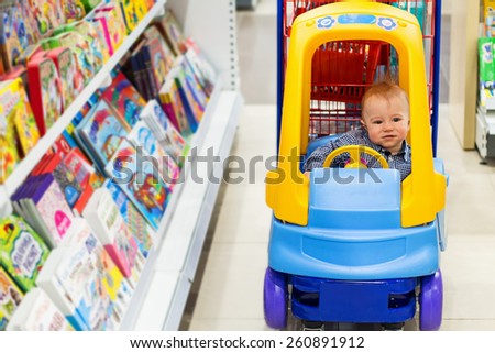 Happy baby in the little toy-car trolley in the kids shop in the bookstore department