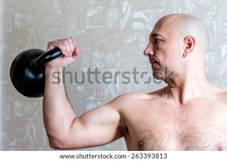 Brawny arm with kettlebell of handsome bold man. Colour, horizontal