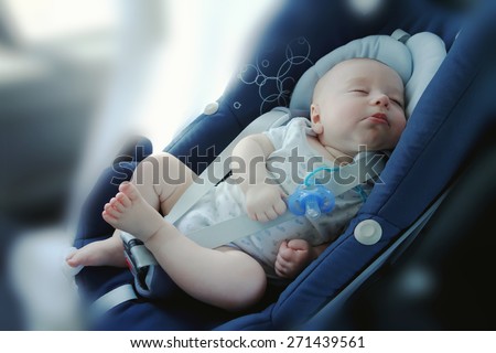 Cute funny baby boy is sleeping in car ?hild safety seat, image with toning, blur background and effect of soft shining sun