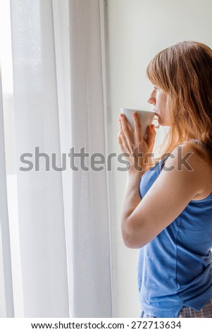 Beautiful  girl with cup of tea or coffee near the window in the morning