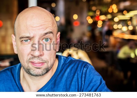 Bold handsome man is distrustfully raising eyebrow as he is surprised with beautiful lights in the background