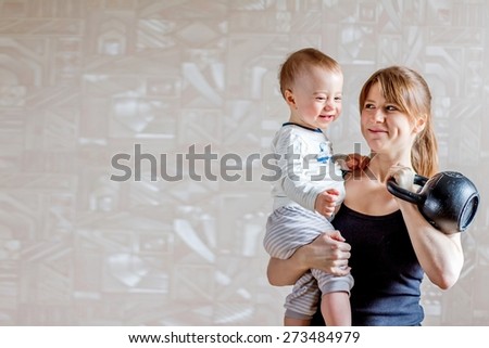 Sportive mother with cute baby boy and kettlebell in hands. Motherhood is not a cause to let oneself go