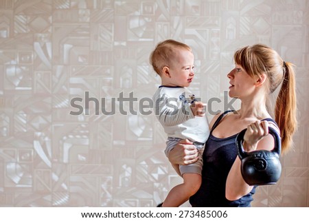 Sportive laughing mother and baby and kettlebell in hands. Motherhood is not a cause to let oneself go
