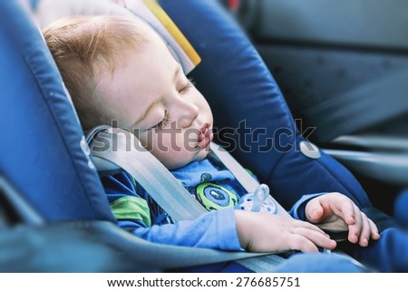 Cute baby boy with long eyelashes sleeping in a car child safety seat. Image with toning, blur background and effect of soft shining sun