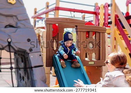 Smiling baby boy is sliding on the chute and his redheaded mother is catching him