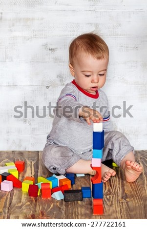 Cute baby boy with concentration is making tower with colorful wooden bricks. Image with selective focus
