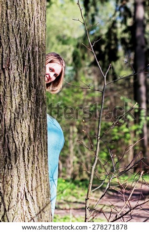Fair hair pregnant woman peeping out of the tree so you can see not only her face but also her belly