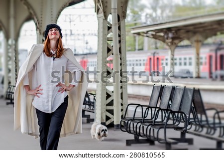 Beautiful smiling ginger hair woman in hat with veil and shih tzu doggy walking on the platform at the Vitebsk railway station in St.-Petersburg, Russia