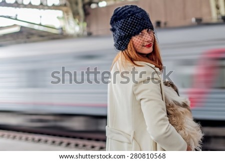 Portrait of elegant young woman with shih tzu dog in hands and moving train in the background at the Vitebsk railway station in St.-Petersburg, Russia. Image with  motion blur.