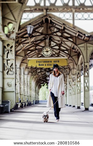 Elegant ginger hair woman is walking with shih tzu dog on the platform under the clock  and inscription 