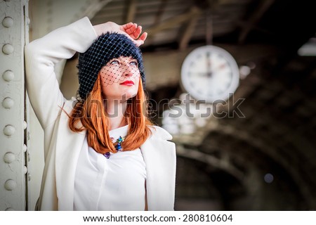 Portrait of stylish beautiful ginger hair woman in hat with veil under the clock at the Vitebsk railway station in St.-Petersburg, Russia.