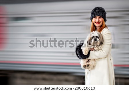 Portrait of smiling young woman with shih tzu dog in hands and moving train in the background at the Vitebsk railway station in St.-Petersburg, Russia. Image with  motion blur.
