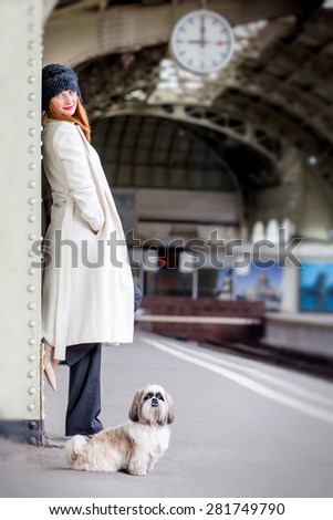 Elegant ginger hair womans with hih tzu dog on the platform under the clock waiting train at the Vitebsk railway station