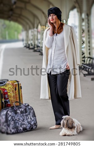 Elegant lady with shih tzu dog and suitcases on the platform speaking on a mobile phone while waiting a train at the Vitebsk railway station in St.-Petersburg, Russia. Image with selective focus